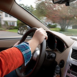 A woman holds the steering wheel of a car while driving down the road.