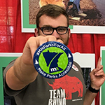 Man holding a button that reads: ”MN Parks For All, Make Parks Accessible.” In the background are photos of people with disabilities enjoying state parks.