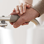 Close up of a man's hand holding on to a walker. A woman's hand rests on top of his.
