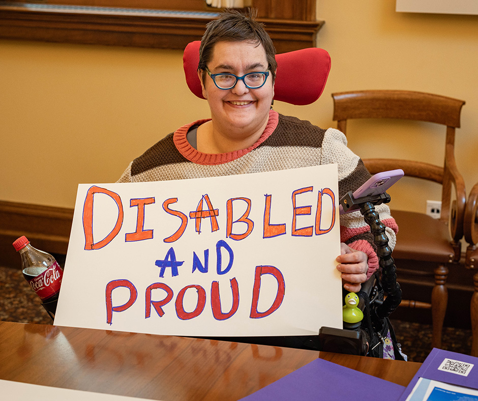 A woman using a wheelchair holds a sign that reads, "Disabled and Proud."