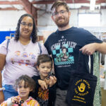 A family visiting the Kandiyohi County Fair. A man holds a "Treat People Like People" tote bag, and two children hold fidget spinners.