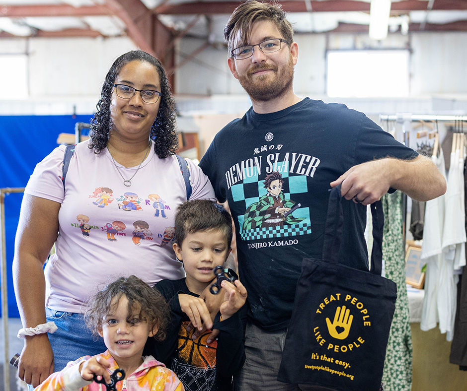 A family visiting the Kandiyohi County Fair. A man holds a "Treat People Like People" tote bag, and two children hold fidget spinners.