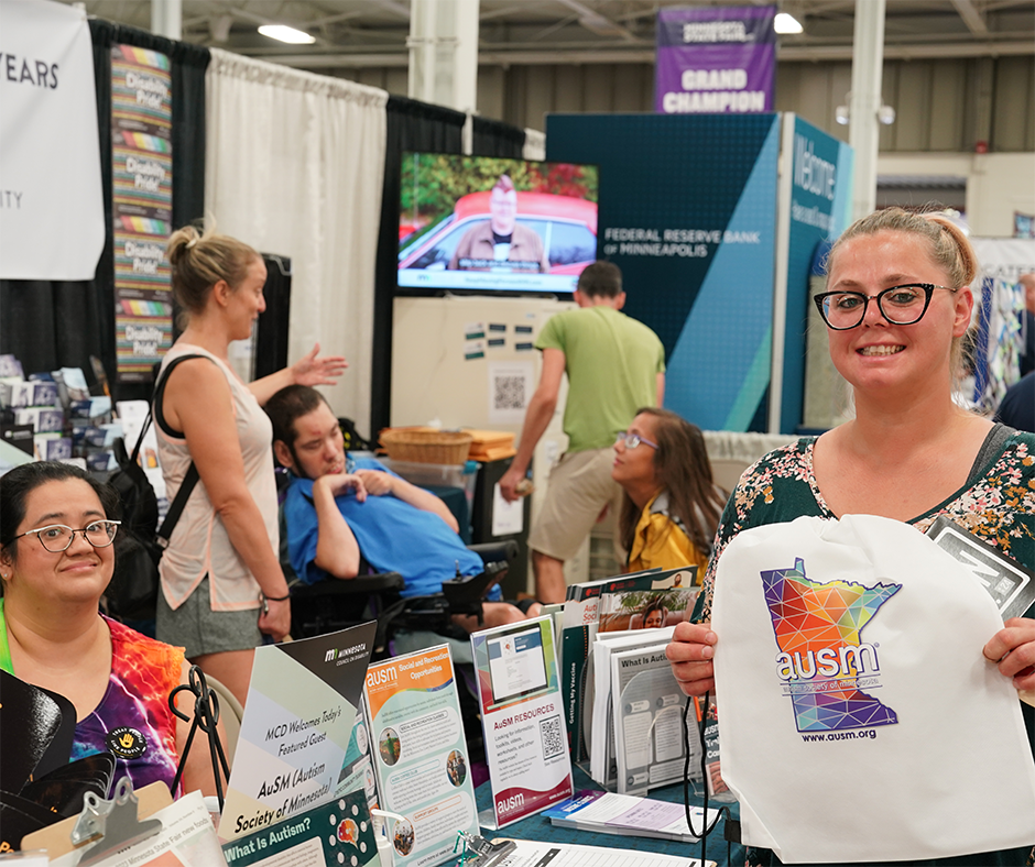 A woman visiting the MCD booth holds up an AuSM bag (Autism Society of Minnesota).