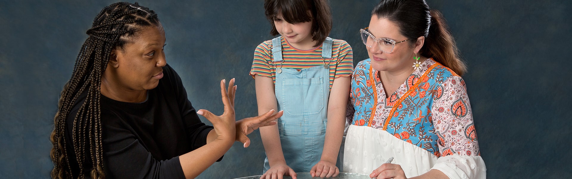 A woman performing sign language for another woman and a young girl