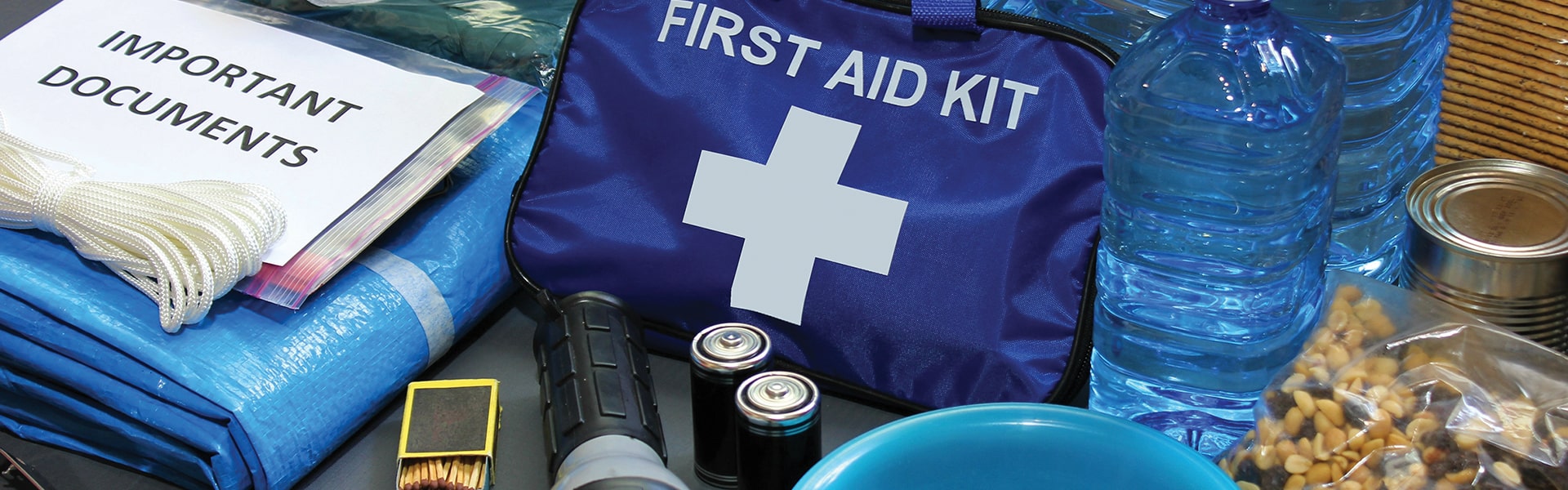 A first aid kit, bottles of water, flashlight, batteries, matchsticks, trail mix, tarps, and important documents.