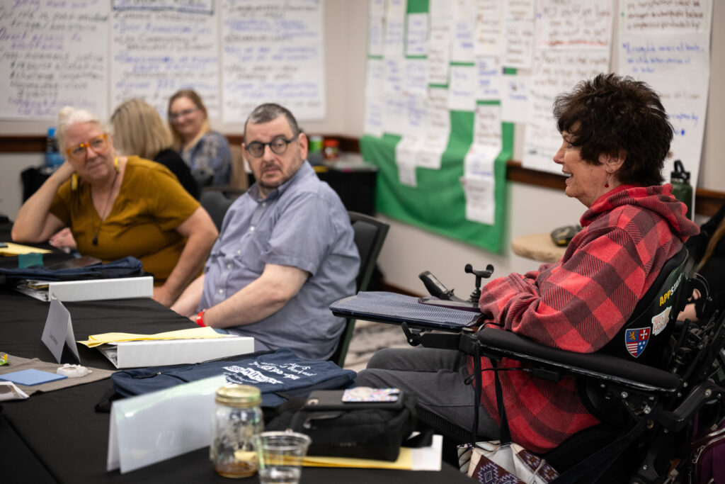 Three people at a conference table, one of them uses a wheelchair.