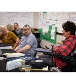 Three people at a conference table, one of them uses a wheelchair.