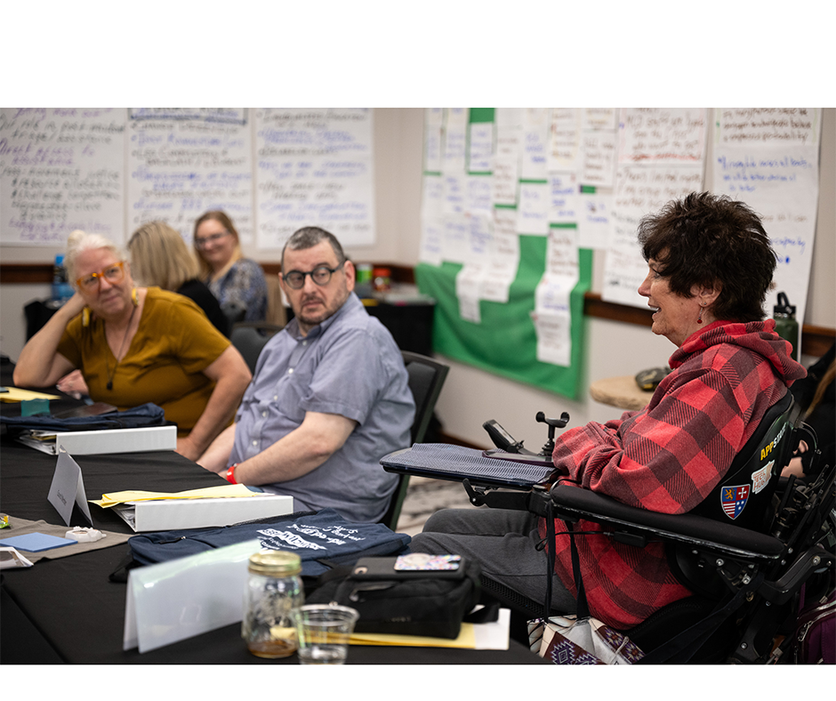 Three people at a conference table, one of them uses a wheelchair.