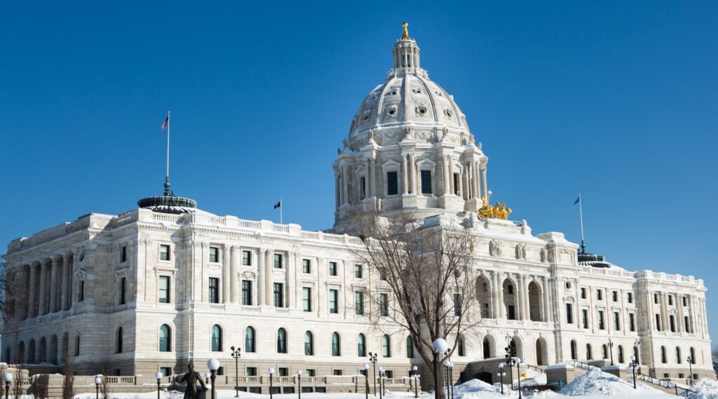 The Minnesota State Capitol building on a sunny winter day. Snow covers the ground, and flags fly on the roof.