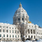 The Minnesota State Capitol building on a sunny winter day. Snow covers the ground, and flags fly on the roof.