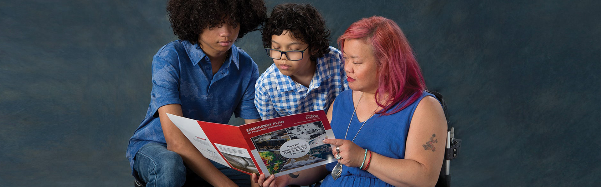 A woman sitting reading an emergency plan to two younger boys.